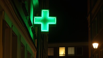 Vibrant neon pharmacy cross illuminates a tranquil, quiet urban neighborhood at night, casting a soft glow.