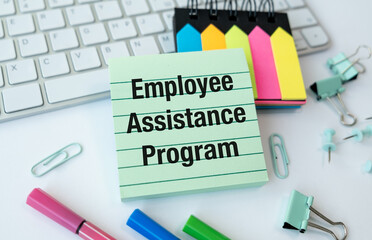 A green piece of paper with the words Employee Assistance Program written on it. The paper is sitting on a desk with a keyboard and a pair of scissors