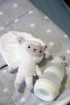 Soft plush lamb toy with baby bottle and pacifier in pastel nursery