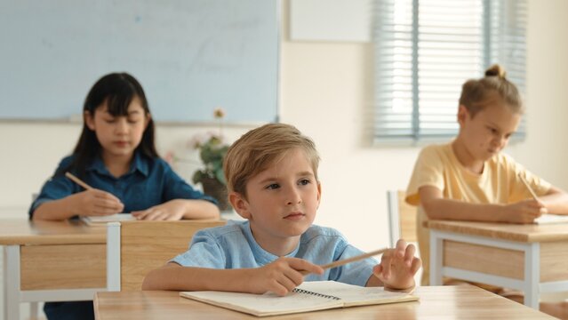 Caucasian boy looking at blackboard while diverse skilled student learning at school and taking a note. Smart child in casual cloth sitting in front of blackboard while children doing test. Pedagogy.