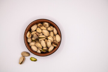 Top down view of a small terracotta dish filled with pistachio nuts on a white background, ideal for illustrating healthy snacks, nutrition, and natural food concepts
