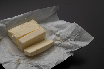 A piece of fresh butter wrapped in wrapping paper on a black background. Spreading butter on bread. Perfect for cooking projects.