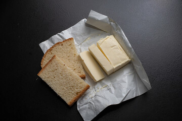 A piece of fresh butter wrapped in wrapping paper on a black background. Spreading butter on bread. Perfect for cooking projects.