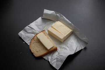 A piece of fresh butter wrapped in wrapping paper on a black background. Spreading butter on bread. Perfect for cooking projects.