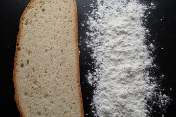 A pile of scattered flour and a piece of fresh bread on a black background. Top view. Making dough from delicious wheat flour. The process of cooking.