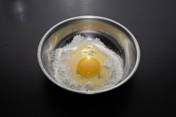 A pile of flour and a broken egg in a bowl. View from above. Making dough from delicious wheat flour. The process of cooking.