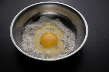A pile of flour and a broken egg in a bowl. View from above. Making dough from delicious wheat flour. The process of cooking.