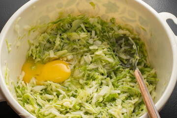 Hand mixing grated zucchini, oats, herbs and egg in a white plate makes a healthy meal. Zucchini pancake batter, zucchini cake. Zucchini pancakes. Vegetarianism. Home cooking process.