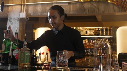 Portrait good looking Asian bartender using jigger measure liquor syrup into mixing glass preparation at luxurious beverage counter bar, neat professional barman costume at nightclub luxury. Vinosity.