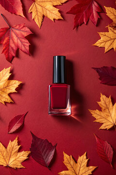 Autumn nail polish bottle surrounded by colorful fall leaves on a red background