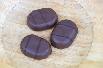Three Glossy Chocolate Candies with Twin Stripes on Wooden Surface