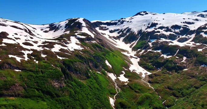 Distancing from the mountain top covered with some snow. Drone footage over the gorgeous rocks on sunny day. Alaska nature.