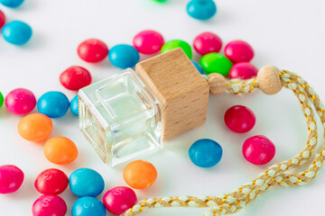 Car air freshener with a transparent bottle, wooden lid and a cord with multi-colored dragees around it.