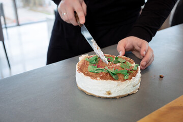 A man cuts a cheesecake with cream and mint garnish. The action takes place at a table, the atmosphere is calm and cozy.