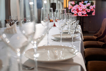 A long table in a restaurant, elegant table setting: white plates, glasses, napkins. In the background, a screen with flowers, soft chairs. An atmosphere of coziness and celebration.