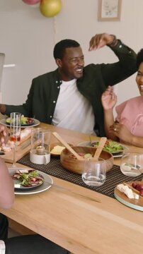Vertical video: Hearing toast, diverse friends clinking rose glasses celebrating at dining table