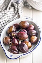 Ripe plums in bowl on white table.