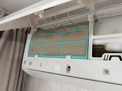 Close up of an air conditioner with a clogged dusty filter and ice formation inside, showing poor maintenance and risk to health and efficiency.