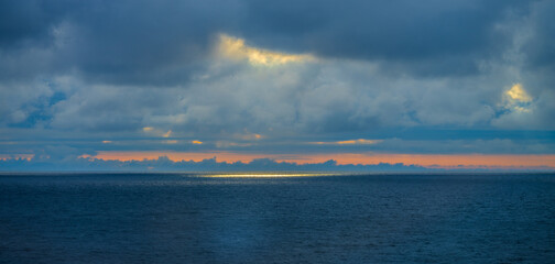 Naklejka premium Sunlight breaking through clouds over distant ocean.