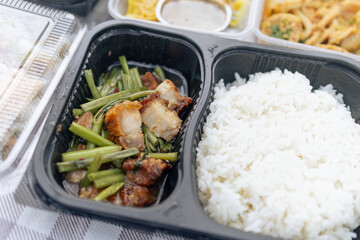 Thai delivery Boxed meal with variety of Thai dishes . A Thai Stir Fried Squid with Curry , Stir Fried Water Mimosa with Crispy Pork on Rice , Pork Dumpling ,