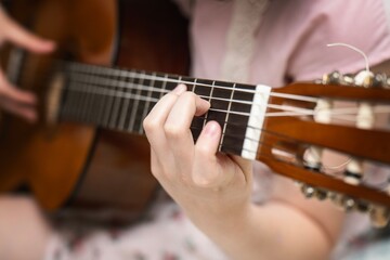 Obraz premium Child's hand learning to play guitar, forming chords on the fretboard during a lesson