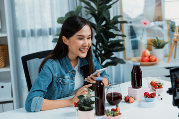 Smiling young beautiful Asian reviewing tasty mixed strawberry and cherry juice detox drinks,...