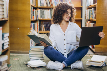 Young student comparing information between laptop and book in library