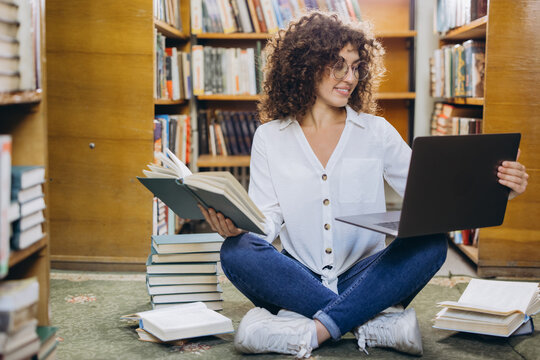 Young student comparing information between laptop and book in library