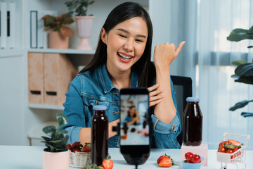 Smiling young beautiful Asian reviewing tasty mixed strawberry and cherry juice detox drinks,...