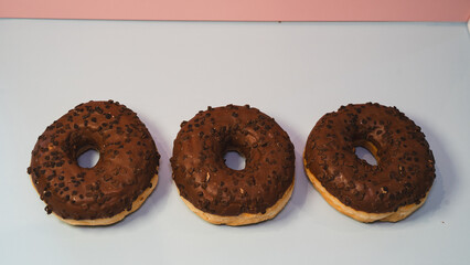 Three rich chocolate donuts with glossy glaze, captured in a close-up to showcase their decadent texture and appeal. Ideal for dessert menus, bakery promotions, and social media content.