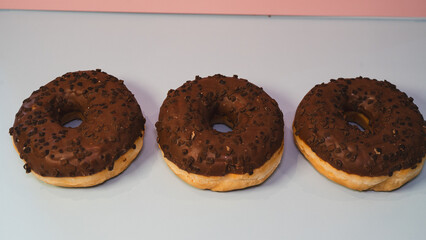 Three rich chocolate donuts with glossy glaze, captured in a close-up to showcase their decadent texture and appeal. Ideal for dessert menus, bakery promotions, and social media content.