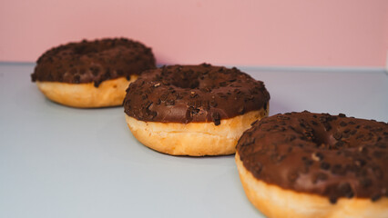 Three rich chocolate donuts with glossy glaze, captured in a close-up to showcase their decadent texture and appeal. Ideal for dessert menus, bakery promotions, and social media content.