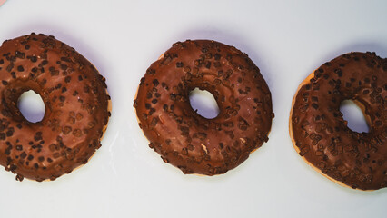Three rich chocolate donuts with glossy glaze, captured in a close-up to showcase their decadent texture and appeal. Ideal for dessert menus, bakery promotions, and social media content.