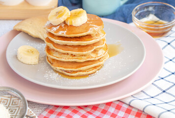 homemade banana pancakes on plate sprinkled powder and honey. Pancakes on the kitchen table against the background of eggs and cups with coffee. Pancake slide with honey topping and fresh bananas