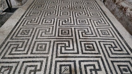 Herculaneum, Italy - 9 January 2025. Intricate floor mosaic with interlocking Greek key designs and central diamond shapes in a Roman bath or villa room.