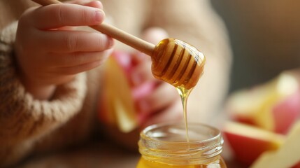 A child's hand drips honey from a wooden dipper into a jar. Slices of red apples are visible in the background. The scene conveys a sense of sweetness and warmth.