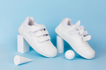 White children's sneakers on blue background. Minimal background