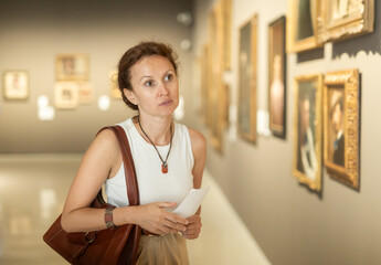 Interested woman in casual clothes exploring paintings in halls of art museum