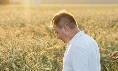 Man in a ripe rye field wearing a white shirt during golden hour, illuminated by warm sunlight. Ideal for themes of agriculture, countryside lifestyle, harvest season, and nature.
