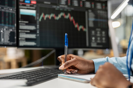 Close up of risk analyst monitoring stock market activity to identify volatility signs, writing down notes. Worker reviews portfolio performance reports, preparing audit for manager - Powered by Adobe