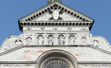 Tympanum and religious sculptures on the upper part of the front gable of Cremona cathedral on a summer day with blue sky, Italy