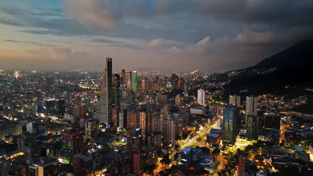 Aerial drone view of skyscrapers lighting up the skyline against the Andean foothills in Bogota, Colombia in the evening