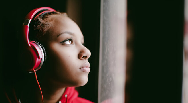 Teenager Black girl listening to music while looking out the window  