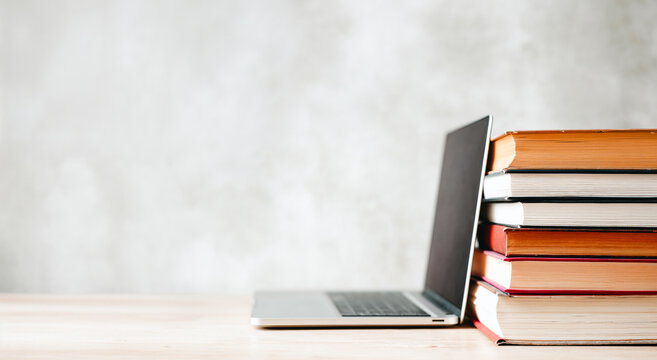 Laptop beside stack of books on wooden desk representing Back to school concept  
