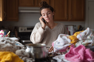 Stressed woman on phone in a cluttered kitchen. Captures the feeling of overwhelm, busy lifestyle, and multitasking. Useful for portraying modern life challenges.