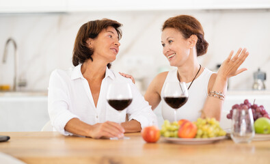 Two girlfriends chatting and drinking red wine in a cozy home kitchen