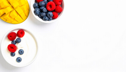 Greek yogurt in white bowls with fresh berries and mango isolated on white background, healthy breakfast, high-protein meal, copy space, top view