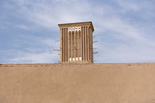 Traditional windcatcher (Badgir) and adobe wall in Yazd desert city of Iran, showcasing historic desert architecture and ancient natural cooling system.