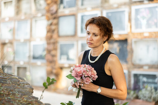Visit to cemetery, woman in mourning clothes grieves for deceased relative. Near grave widow grieves and prays for soul of deceased relative, moment of remembrance, to pay tribute to memory