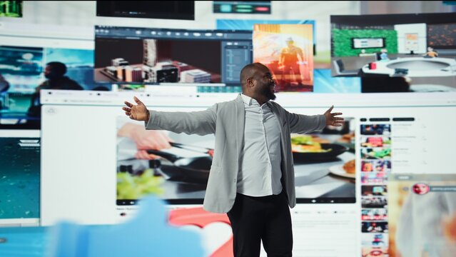 Delighted man with open arms facing video wall expressing happiness, enjoying endless entertainment clips. Cheerful african american viewer enjoying access to endless streaming options, camera A